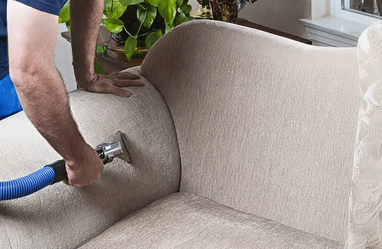 Professional upholstery cleaner deep-cleaning a fabric sofa with a handheld extraction tool and hose, Phoenix, AZ.